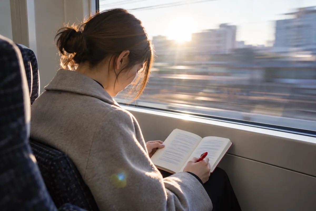朝の電車の窓際でノートを読み返している人