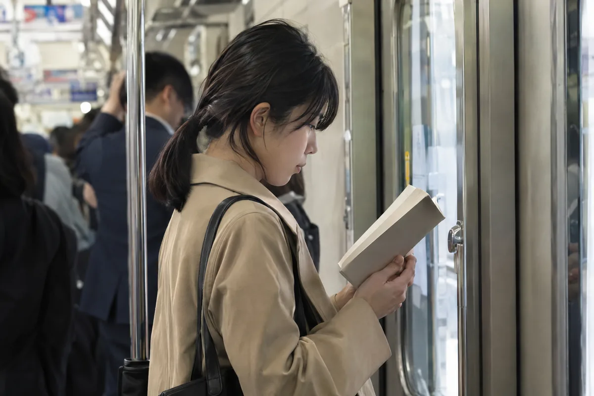 朝の電車のドアのそばで本を読む人
