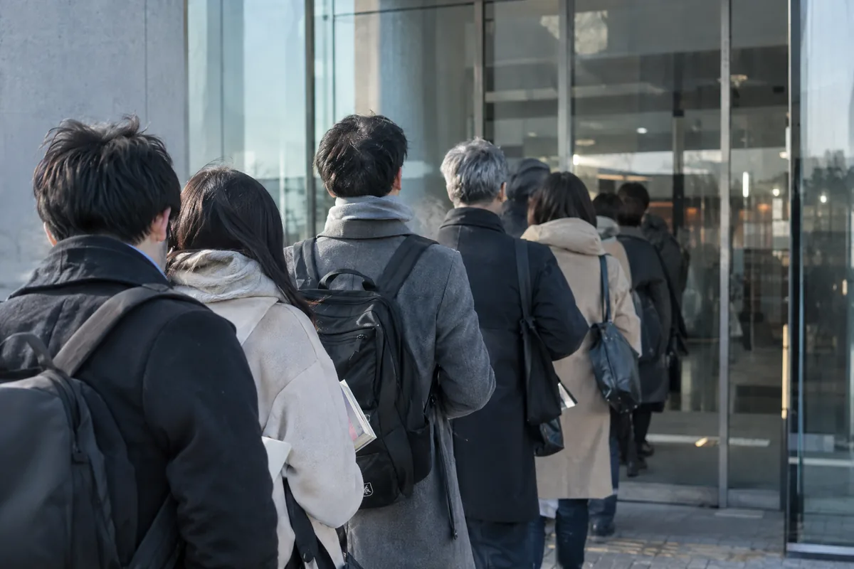 朝の試験会場の入口に並ぶ受験者の後ろ姿